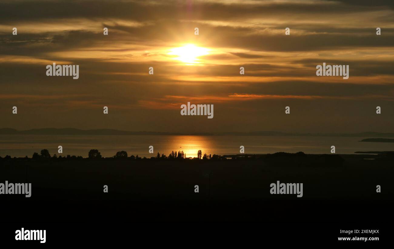 Sonnenuntergang auf der Insel Rügen mit Blick auf den großen Jasmund Bodden. Bewölkt, trüb und daher verschleiert, aber sehr schön und romantisch. Stockfoto