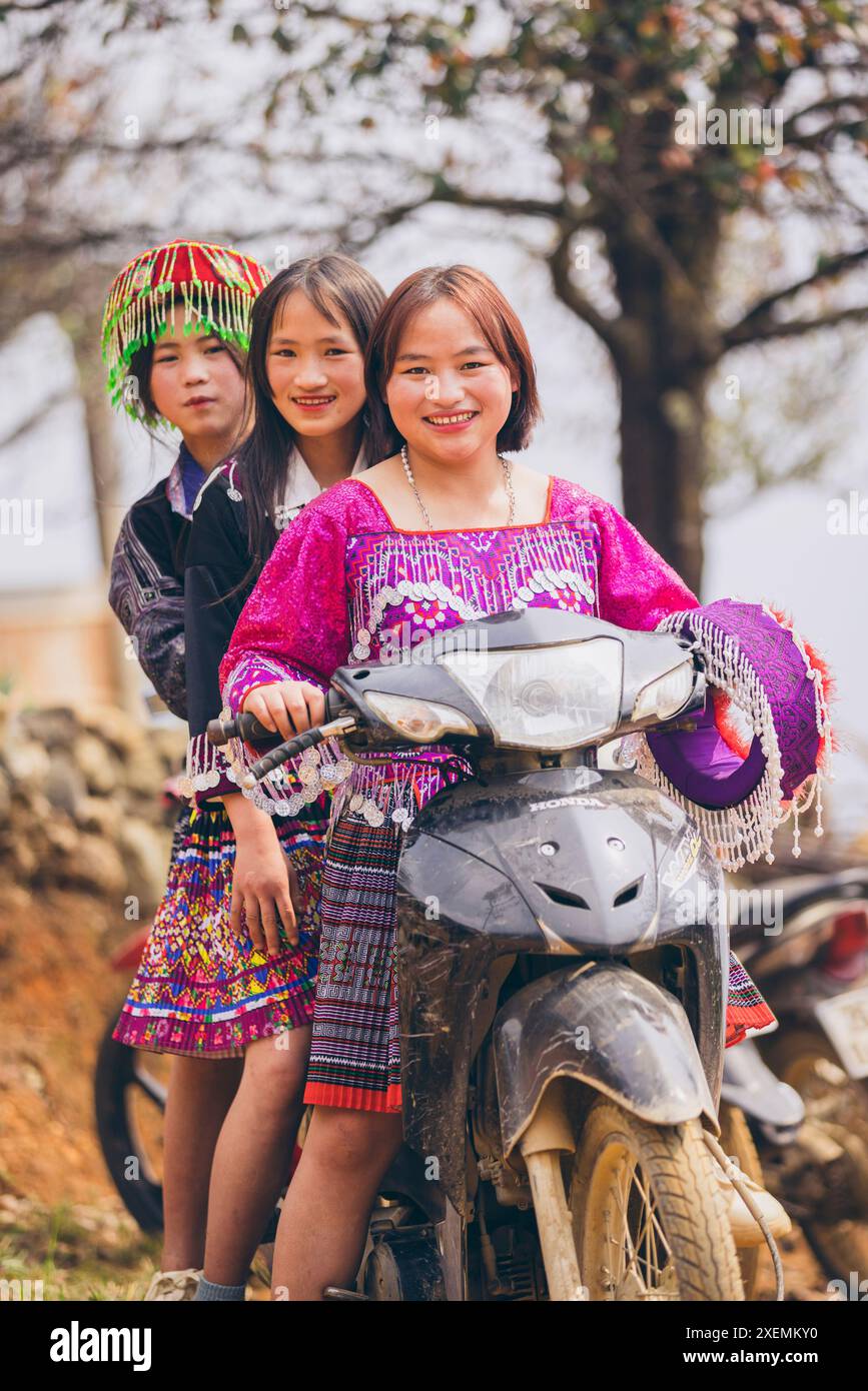 Drei junge vietnamesische Frauen, die zusammen auf einem Motorrad posieren, in traditionellen Kleidern; Ban Nam Nghiep, Muong La, Son La, Vietnam Stockfoto