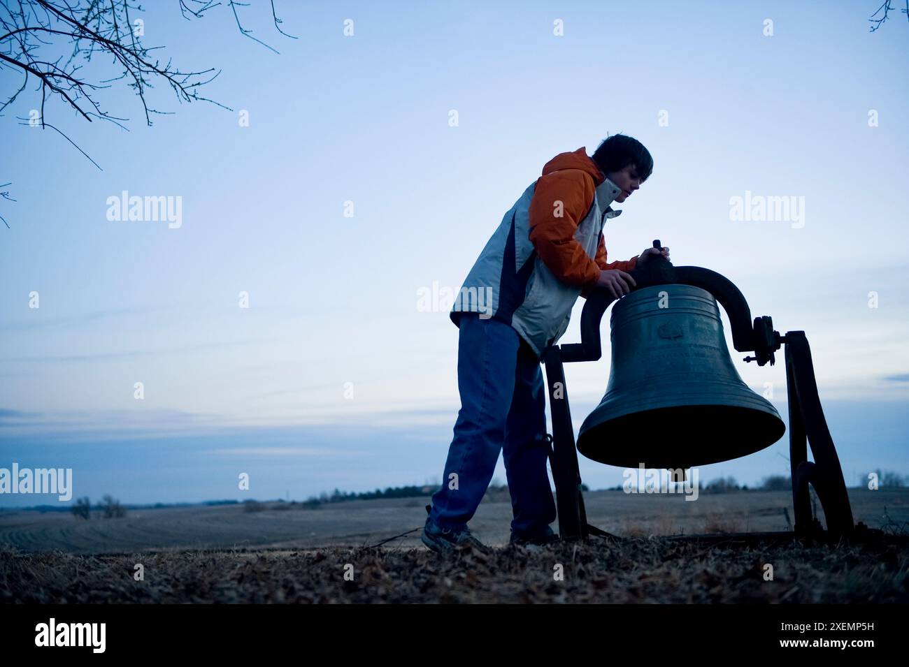 Silhouette eines Teenagers, der eine alte Glocke läutet, auf einer Farm in der riesigen Counryside in Nebraska, USA; Cortland, Nebraska, USA Stockfoto