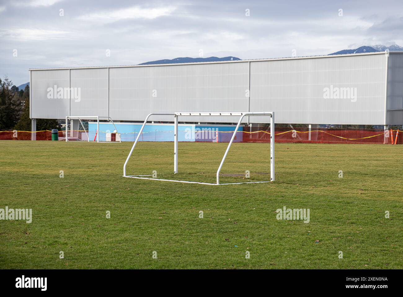 Leeres Fußballfeld (Fußballfeld) mit Metalltorpfosten auf grünem Gras, vor einem Hintergrund von Gebäuden und Bergen. Stockfoto