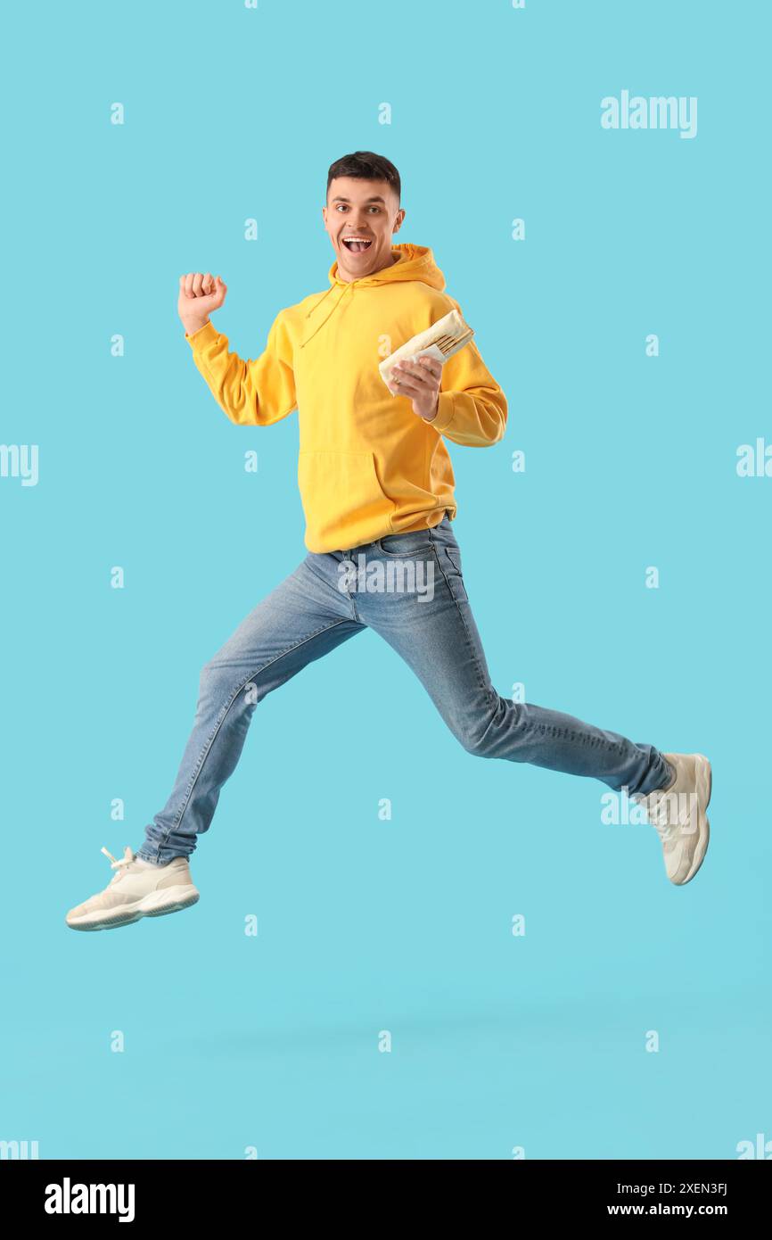 Springender junger Mann mit leckerem Döner-Kebab auf blauem Hintergrund Stockfoto