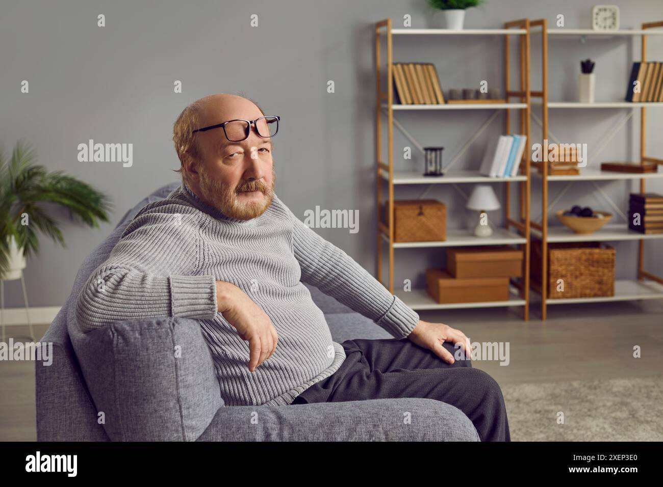 Porträt eines ernsthaften Seniorenmannes, der auf der Couch im Wohnzimmer sitzt Stockfoto