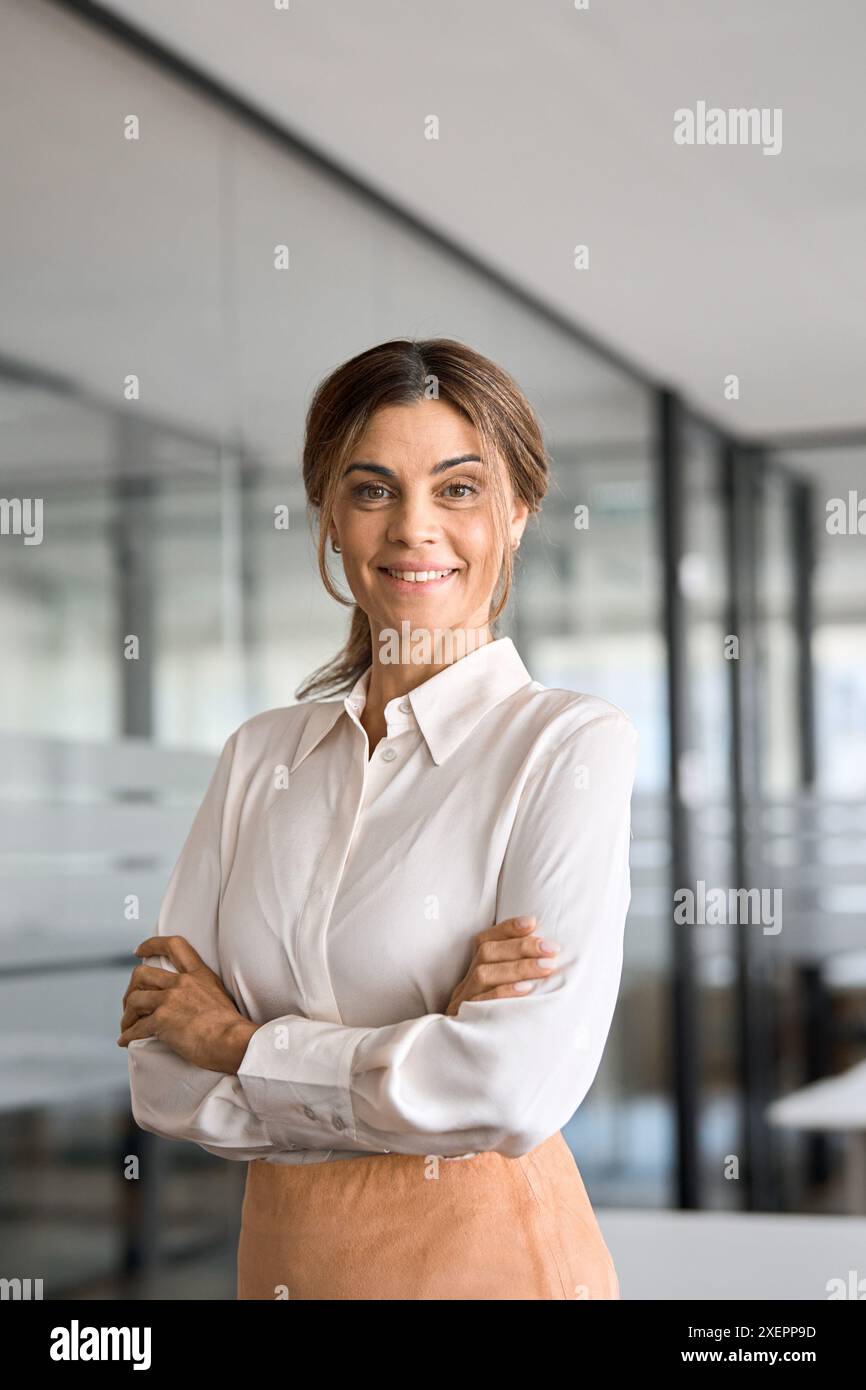 Reife Geschäftsfrau, die im Büro steht und auf die Kamera blickt, vertikales Porträt. Stockfoto