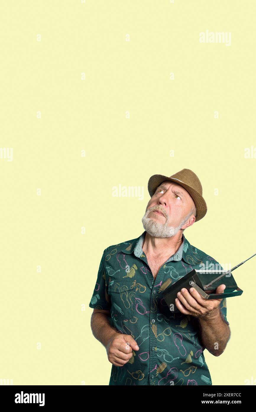 Ein Gentleman mit Hut hört ein altes Radio auf gelbem Hintergrund. Eindrücke von den Nachrichten im Radio. Stockfoto