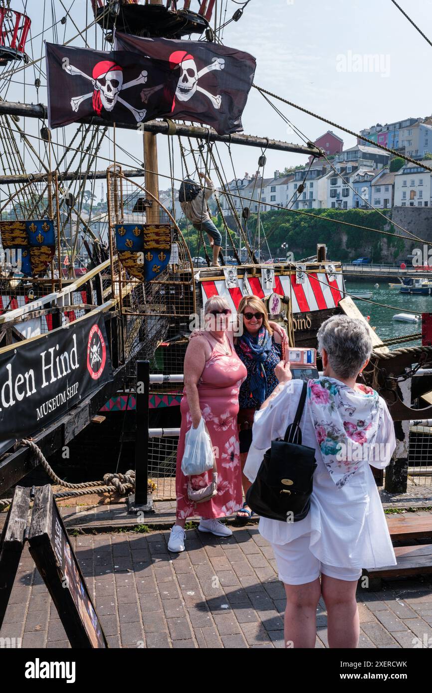 Touristen posieren für ein Foto neben der Nachbildung von Sir Francis Drakes Golden Hind im Brixham Harbour, Devon. Stockfoto