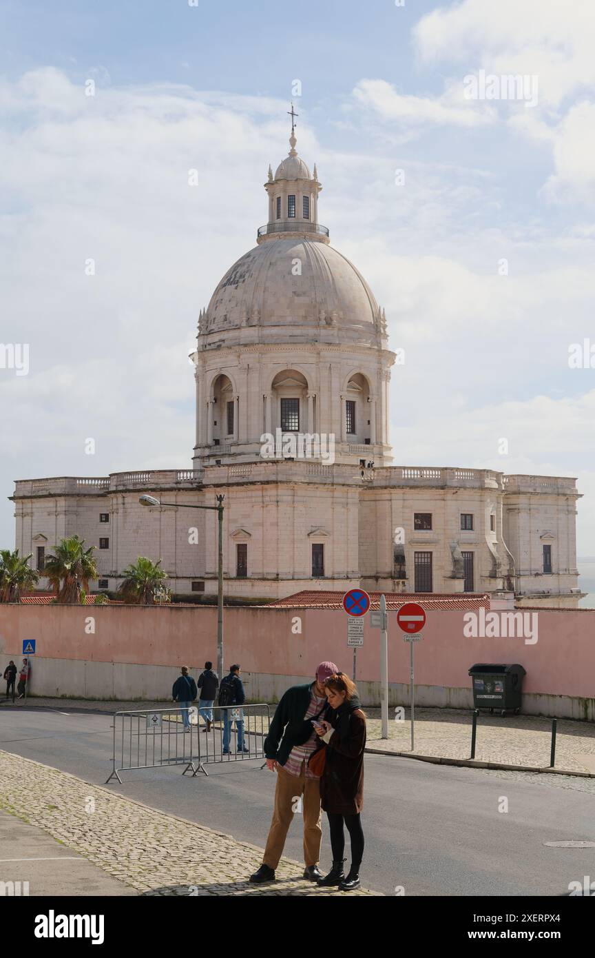 Paare, die auf Telefone im Vordergrund schauen, die Panteão Nacional (Igreja de Santa Engrácia) mit ihrer beeindruckenden Kuppel im Hintergrund Stockfoto