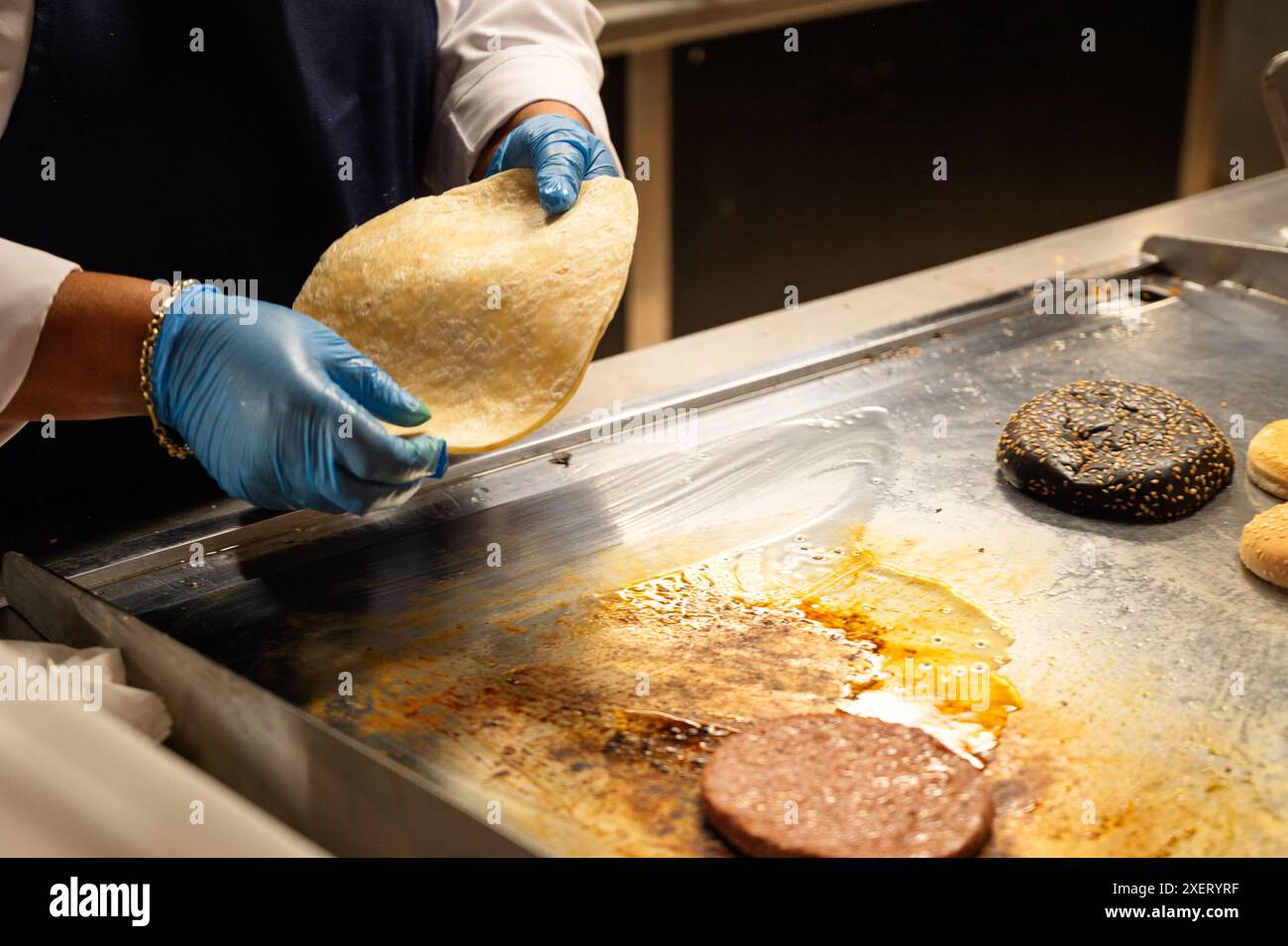 Eine Person kocht Essen auf einem Grill. Das Essen ist ein Taco und ein Hamburger. Die Person trägt Handschuhe Stockfoto