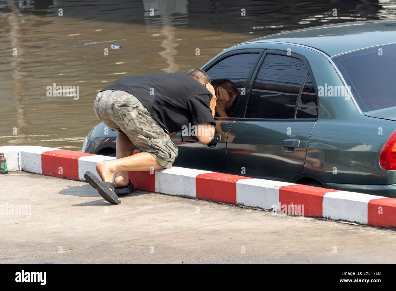 Ein Mann blickt in ein Auto, das in einer überfluteten Straße geparkt ist Stockfoto