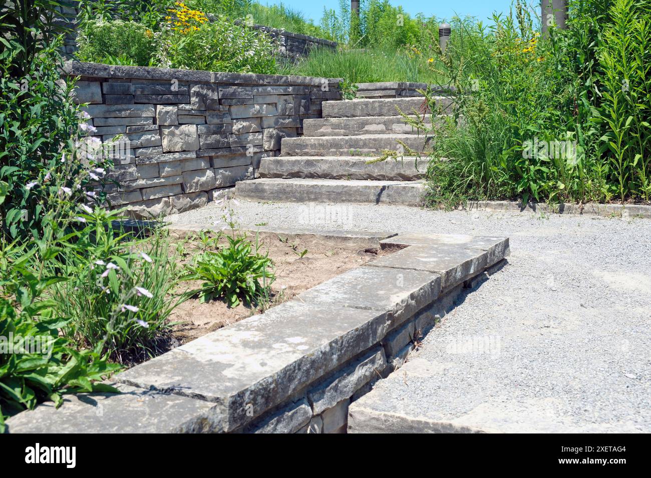 Formelle luxuriöse Landschaftsgestaltung mit Stützmauer aus Naturstein und Ummantelung, breiten Stufen und Landung in einem naturbelassenen Schmetterlingsgarten. Stockfoto