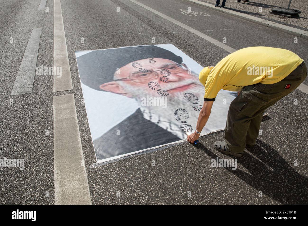 Berlin, Deutschland. Juni 2024. Ein Mann verbreitet ein Poster des iranischen Führers mit Fußabdrücken im Gesicht. Tausende iranischer Exilanten und Kritiker der iranischen Regierung versammelten sich, um gegen die jüngsten Präsidentschaftswahlen zu protestieren, von denen sie behaupten, sie seien manipuliert worden, um Kandidaten zu bevorzugen, die den herrschenden Klerikern loyal sind. Unter dem Motto "Freier Iran " versammelten sich Demonstranten auf dem Bebelplatz in Berlin und verurteilten das, was sie als Scheinwahlprozess in ihrer Heimat wahrnahmen. (Kreditbild: © Michael Kuenne/PRESSCOV via ZUMA Press Wire) NUR REDAKTIONELLE VERWENDUNG! Nicht für kommerzielle ZWECKE! Stockfoto