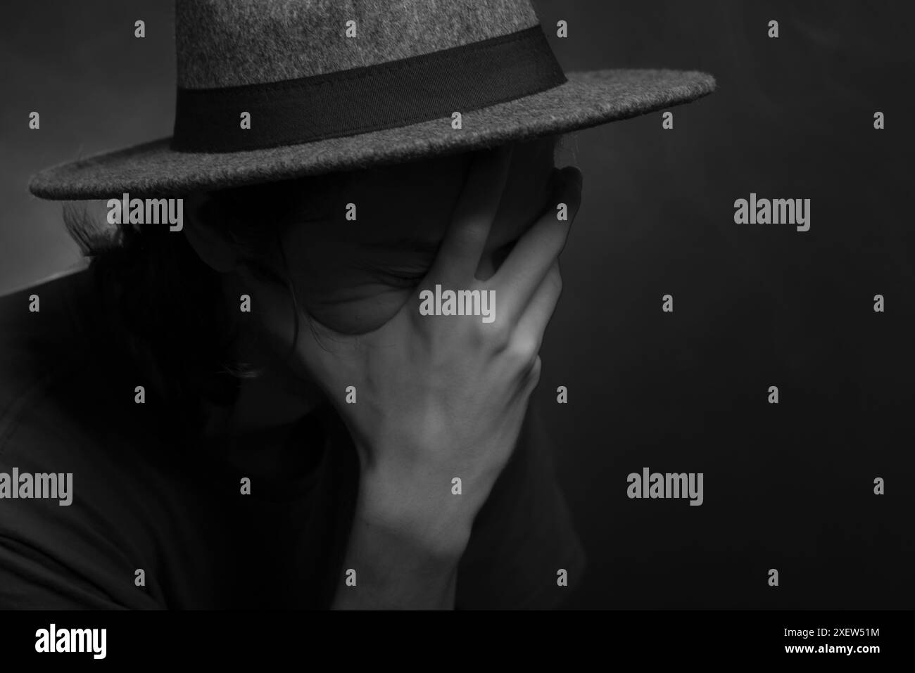 Nahaufnahme eines schwarz-weißen Portraits eines nachdenklichen jungen Mannes mit Hut. Isoliert auf rauchigem Hintergrund. Stockfoto