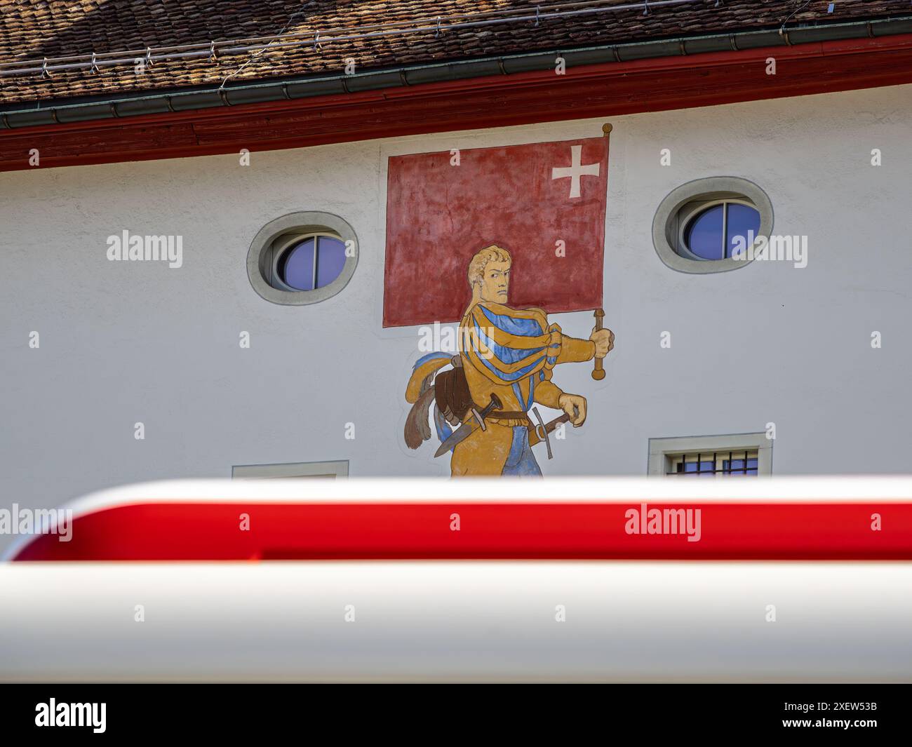 Schwyz, Schweiz - 18. Juni 2024: Mittelalterliche Figur mit roter Flagge des schweizer Kantons Schwyz, Fassade des Schweizerischen Nationalmuseums. Stockfoto