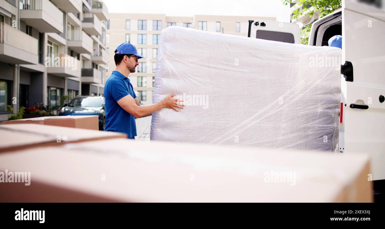 Engagierte Umsteiger in Aktion: Fleißige Männer, die die eingewickelte Matratze aus dem Truck entladen, bieten einen erstklassigen Lieferservice in der geschäftigen City Street. Stockfoto