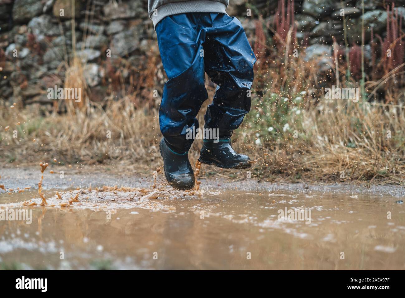 Ein Kind springt in den Regen und spritzt überall Wasser. Die Szene ist verspielt und fröhlich, während das Kind den Regen genießt und Spaß hat Stockfoto