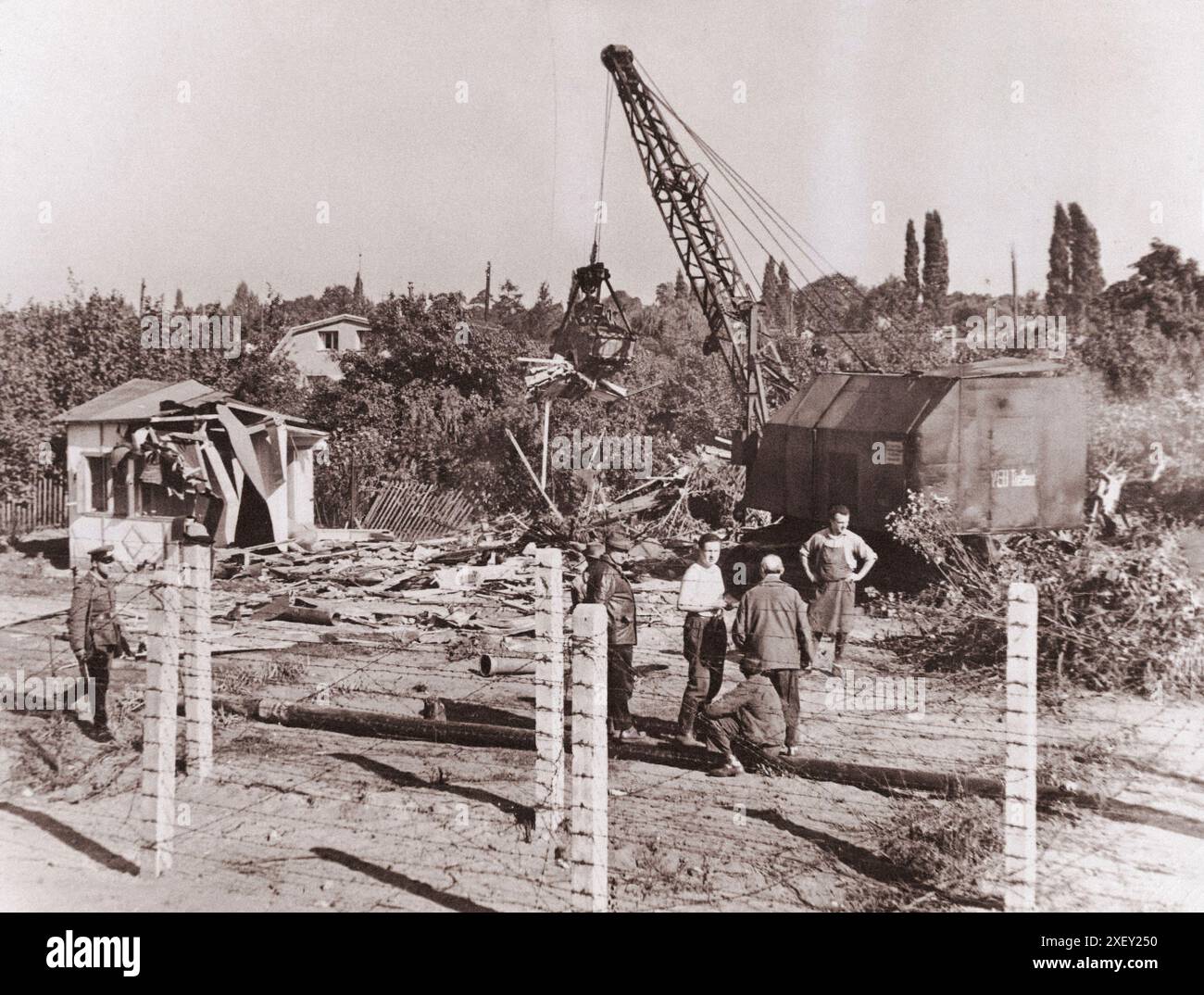 Vintage-Foto der Berliner Krise von 1961: Mauerbau. Unter dem Auge eines kommunistischen „Volkspolizisten“ zerstören Ost-Berliner Arbeiter mit Power Shovel eines von mehreren Hütten und Einfamilienhäusern entlang einer spärlich besiedelten Strecke der Ost-West-Berliner Grenze. Ostdeutschland. Oktober 1961 Stockfoto