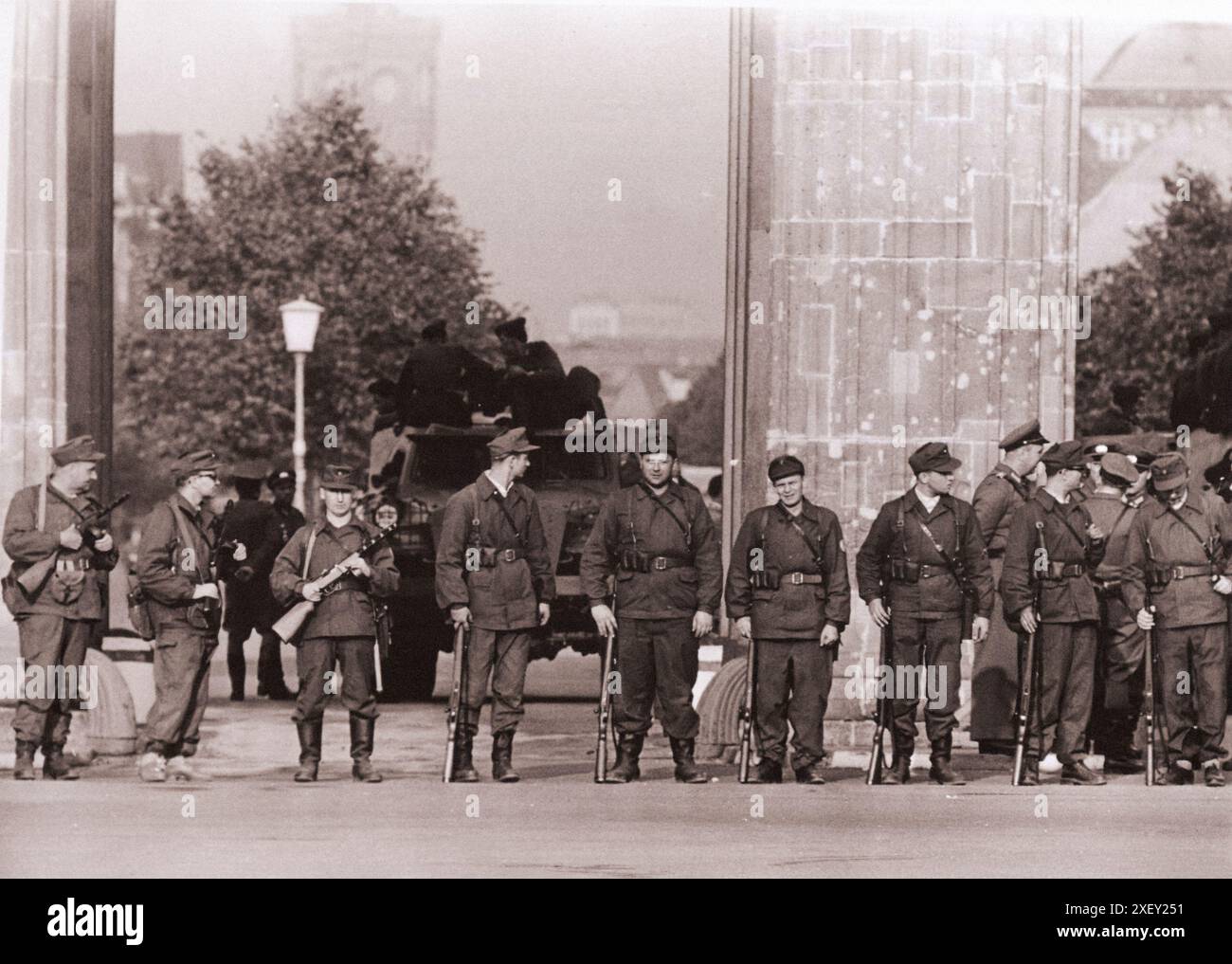 Vintage-Foto der Berliner Krise von 1961: Mauerbau Ein Trupp der Ost-Berliner Arbeitermiliz mit Maschinenpistolen steht Schulter an Schulter vor dem Brandenburger Tor. Hinter ihnen, die den Durchgang blockiert, befindet sich Ein kommunistischer Panzerwagen. Berlin, August 1961 Stockfoto