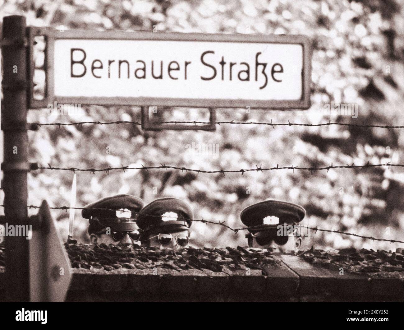 Vintage-Foto der Berliner Krise von 1961: Mauerbau. Drei kommunistische „VOLPO“, DDR-Polizei, strecken sich aus, um einen Blick über eine Friedhofsmauer zu werfen, die zufällig entlang der West-Berliner Grenze verläuft. West-Berlin. 1961 Stockfoto