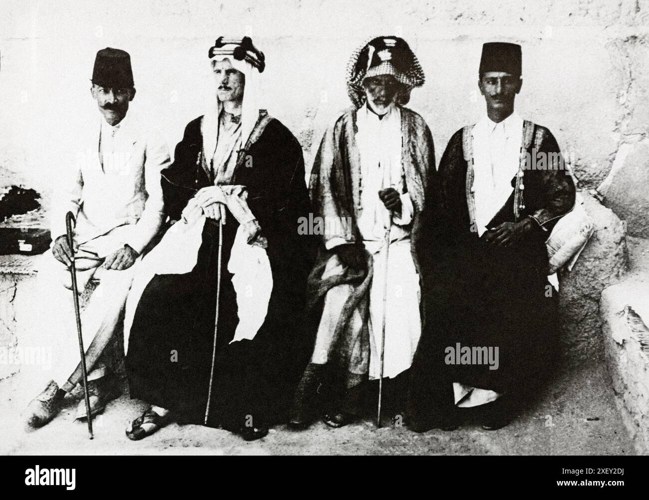 Vintage-Archivfoto eines westlichen Agenten in lokaler Tracht mit zwei türkischen Offizieren und einem alten arabischen Mann. 1916-1918 dieses Foto bezieht sich auf die arabische Revolte von 1916–1818, ein wichtiges Operationstheater während des Ersten Weltkriegs, indem die Briten die Revolte gegen die osmanische Herrschaft unterstützten, versuchten sie, das Osmanische Reich zu schwächen, das mit Deutschland und Österreich-Ungarn in Einklang stand. Die Araber ihrerseits hofften, die Unabhängigkeit zu sichern und ein vereintes Reich zu schaffen, das die Region von Aleppo, Syrien bis Aden, Jemen umfasste. Die Fotografien zeigen viele der Protagonisten in diesem politischen und militärischen Stru Stockfoto