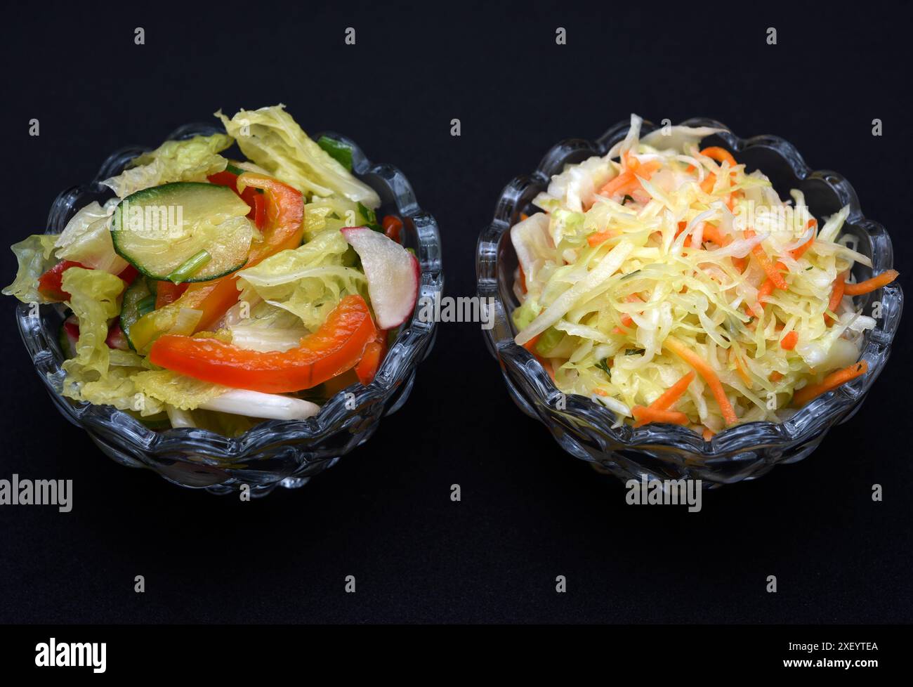 Gemüsesalat in einer Salatschale aus Glas auf schwarzem Hintergrund. Eine Portion Gemüsesalat. Stockfoto