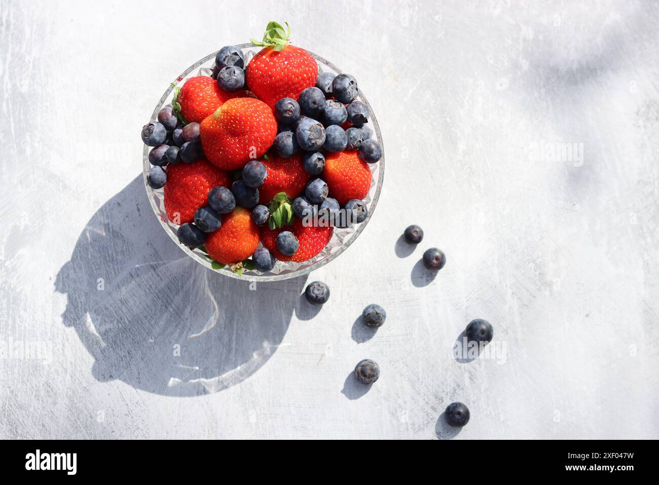 Erdbeeren und Heidelbeeren in einer Glasschale auf grauem Hintergrund mit Platz für Text. Fresh-Konzept. Stockfoto