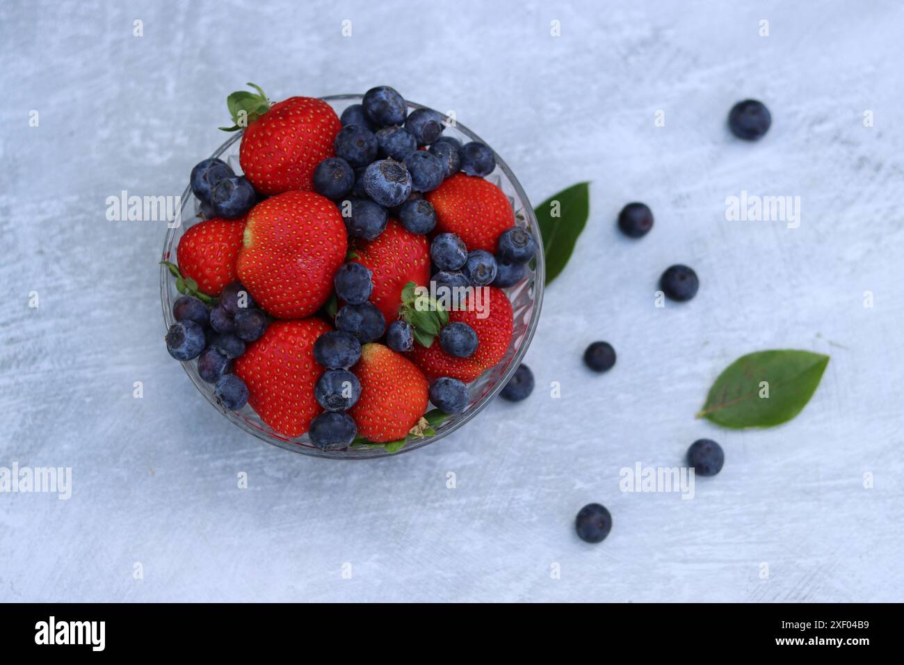 Erdbeeren und Heidelbeeren in einer Glasschale auf grauem Hintergrund mit Platz für Text. Fresh-Konzept. Stockfoto