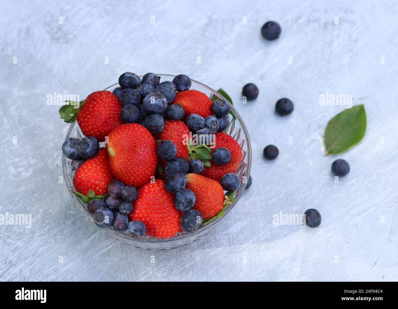 Erdbeeren und Heidelbeeren in einer Glasschale auf grauem Hintergrund mit Platz für Text. Fresh-Konzept. Stockfoto