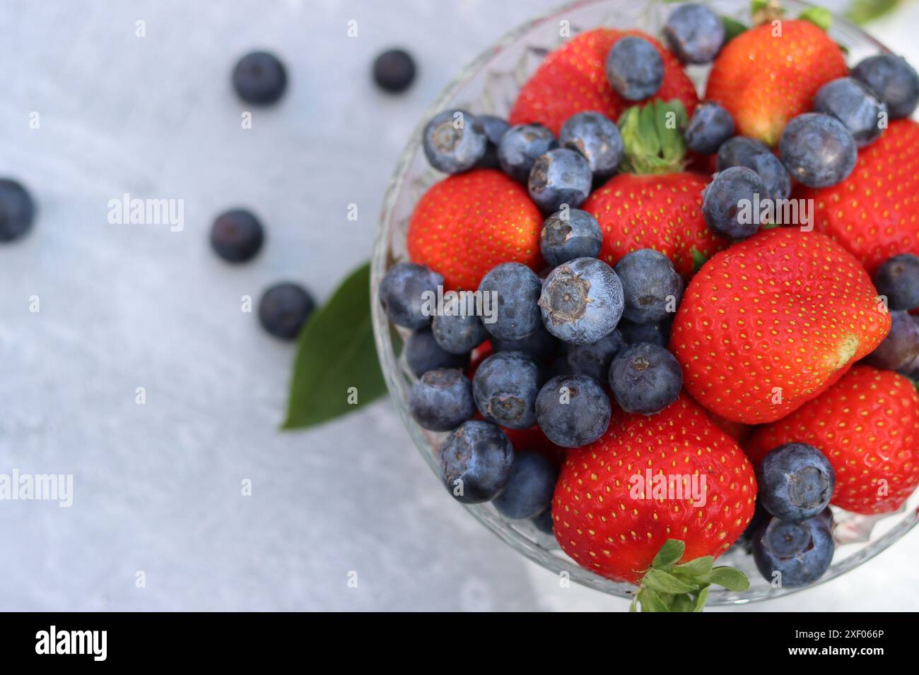 Erdbeeren und Heidelbeeren in einer Glasschale auf grauem Hintergrund mit Platz für Text. Fresh-Konzept. Stockfoto