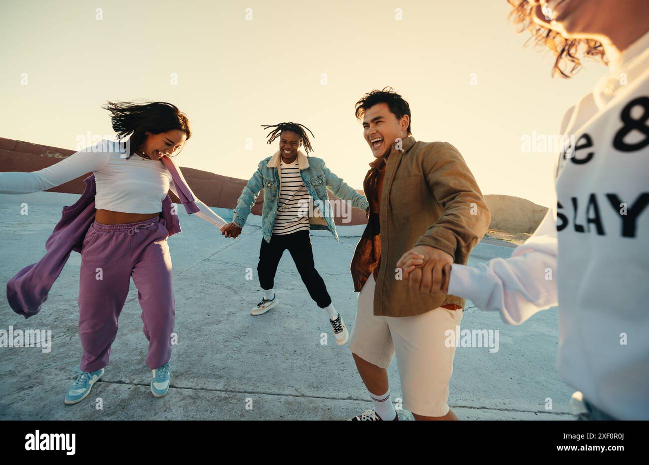 Eine Gruppe von Freunden tanzt und genießt einen lustigen, spontanen Moment im Freien bei Sonnenuntergang. Ihre ehrlichen und fröhlichen Ausdrücke einfangen. Stockfoto