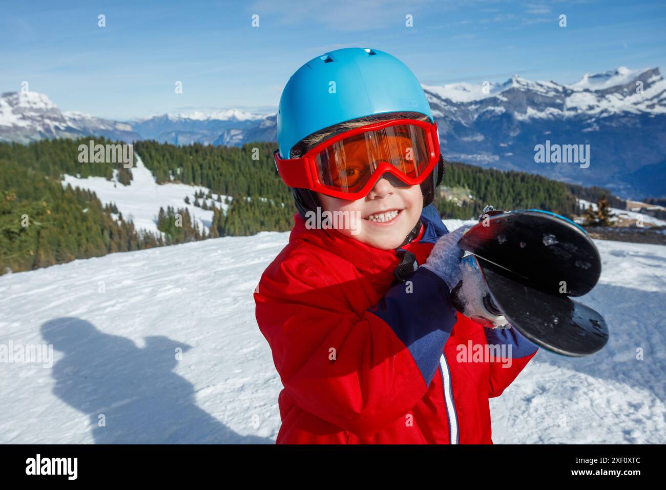 Ein Junge in roter Jacke, der Skier auf den Schultern hält Stockfoto