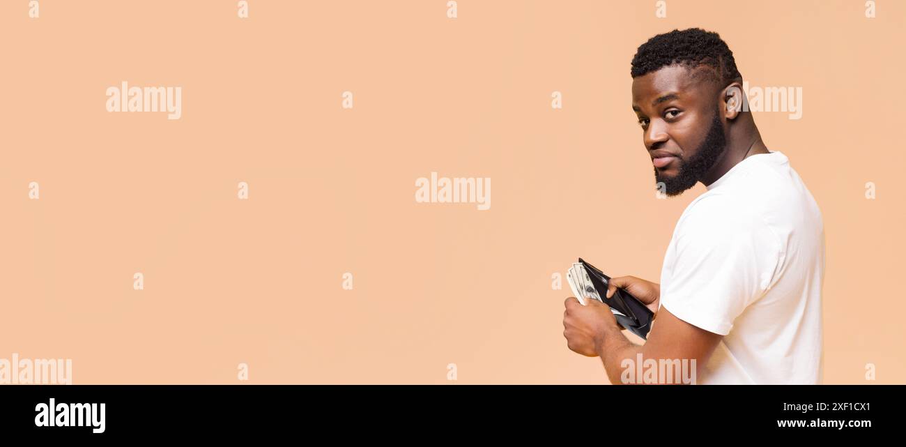 Afroamerikaner, Der Geldbörse Mit Bargeld Gegen Beige-Hintergrund Hält Stockfoto