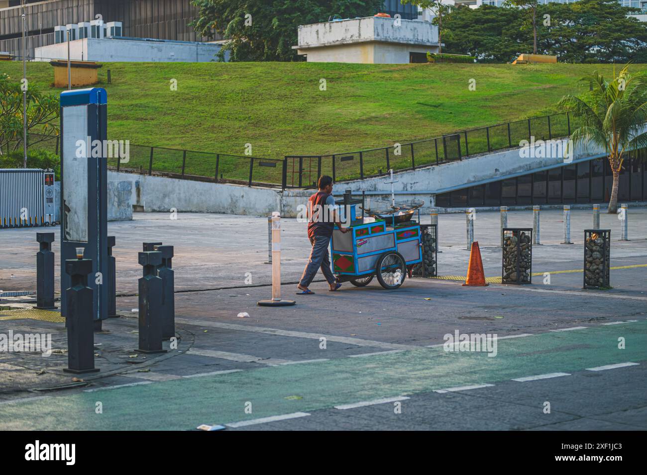 Jakarta, Indonesien - 11. Mai 2024. Ein junger indonesischer Mann, voller Energie, schiebt seinen blau gefärbten Lebensmittelkarren eine Stadtstraße hinunter. Er ist eifrig, anzufangen Stockfoto