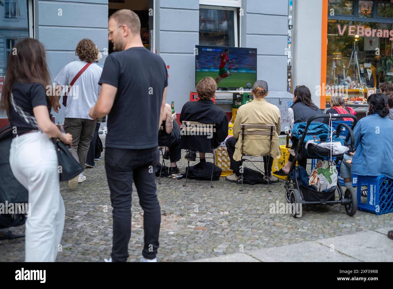 Vor einem Späti in der Oderberger Straße in Berlin-Prenzlauer Berg verfolgen Fußballfans das Spiel Türkei gegen Portugal anlässlich des Fußballeuropameisterschaft UEFA EURO 2024. / Fußballfans sehen das Spiel zwischen der Türkei und Portugal vor einem Late-Night-Shop in der Oderberger Straße in Berlin-Prenzlauer Berg während der Fußball-Europameisterschaft UEFA EURO 2024. UEFA Fußball-Europameisterschaft - Fußballfans *** Fußballfans sehen das Spiel zwischen der Türkei und Portugal vor einem Late Night Store in der Oderberger Straße in Berlin Prenzlauer Berg während der Fußball-Europameisterschaft U Stockfoto