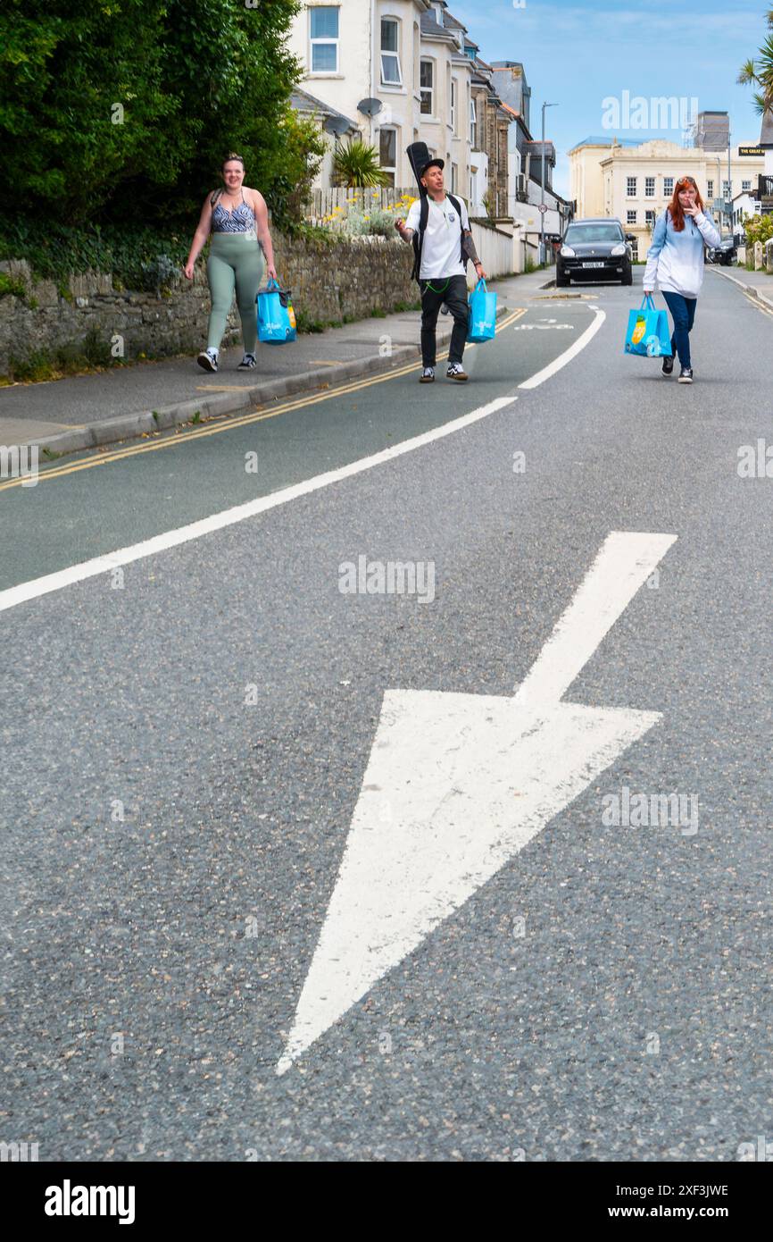 Drei Urlauber, die in Newquay im britischen Cornwall auf einer Straße mit blauen Tragetaschen unterwegs sind. Stockfoto
