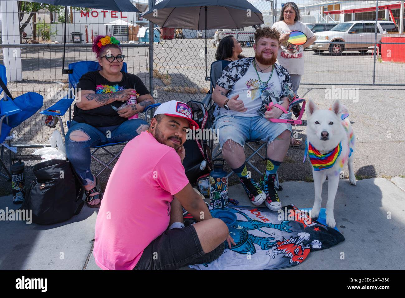 Eine Gruppe, drei Personen und ein Hund sitzen auf dem Gehweg der Route 66 und beobachten die Pride Parade 2024 in Albuquerque, New Mexico, USA. Stockfoto