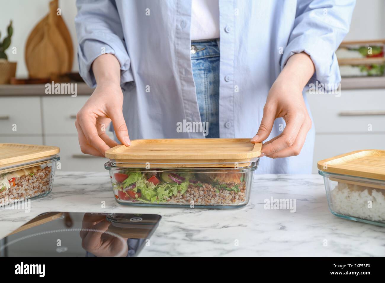 Gesunde Ernährung. Frau schließt Glasbehälter mit Mahlzeit an weißem Marmortisch, Nahaufnahme Stockfoto