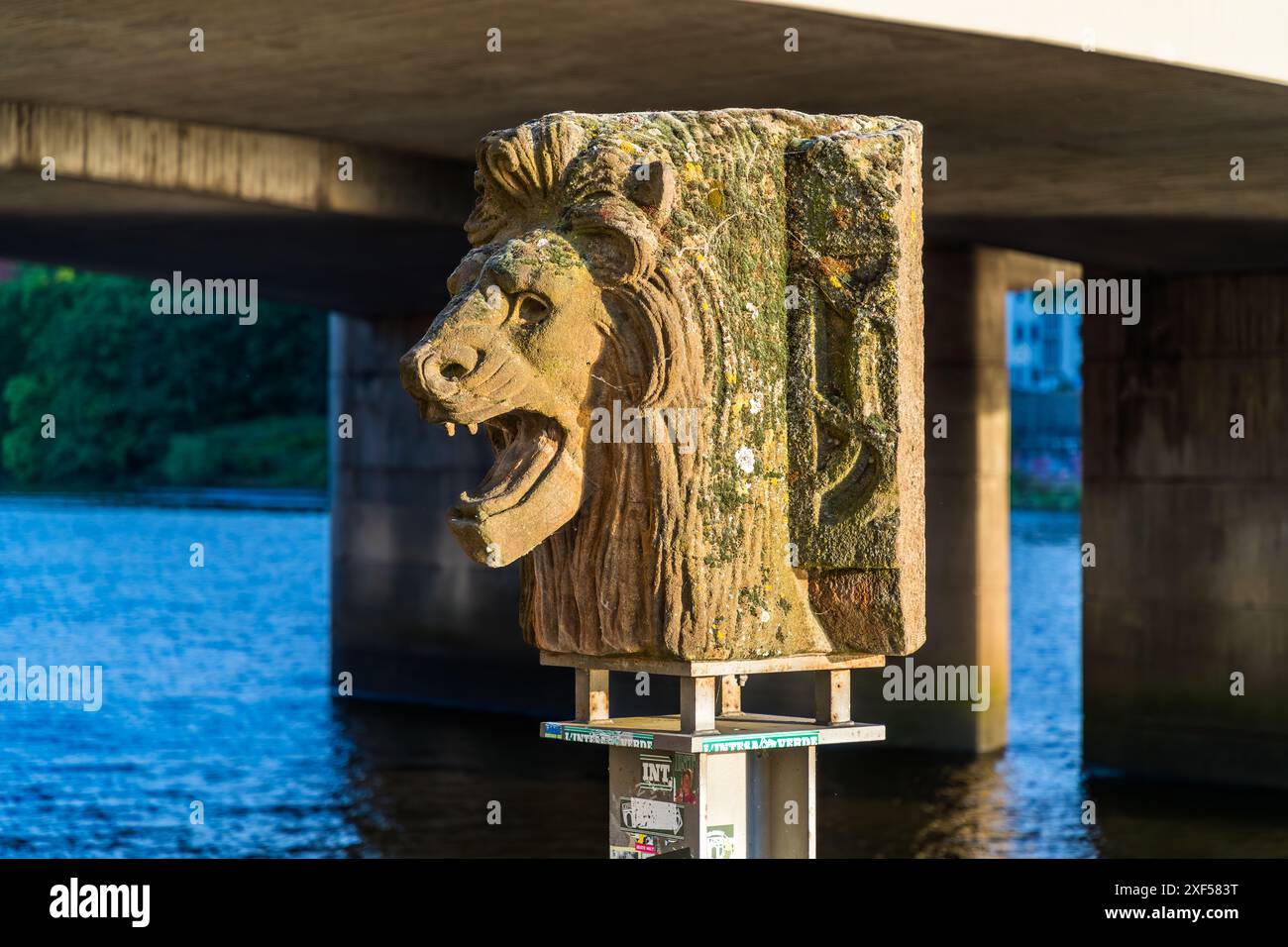 Der Steinkopf des Löwen an der Weser-Promenade in Bremen erinnert an die Große Weserbrücke von 1893, die im April 1945 von den Nazis gesprengt wurde. Der Löwenkopf stürzte in den Fluss und lag jahrzehntelang versteckt. Im Jahr 1998 wurden zwei der vier Sandstein-Löwenköpfe, die von den Pfeilern der Brücke gefallen waren, zufällig wiedergefunden. Er wird nun auf einem Pfosten unter der Wilhelm-Kaisen-Brücke, dem Nachfolger der Kreuzung, ausgestellt. Bremen, Deutschland. Stockfoto