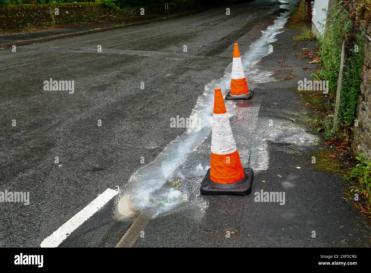 Wasser strömt aus einem undichten Rohr in der Bridge Street, New Mills, Derbyshire Stockfoto