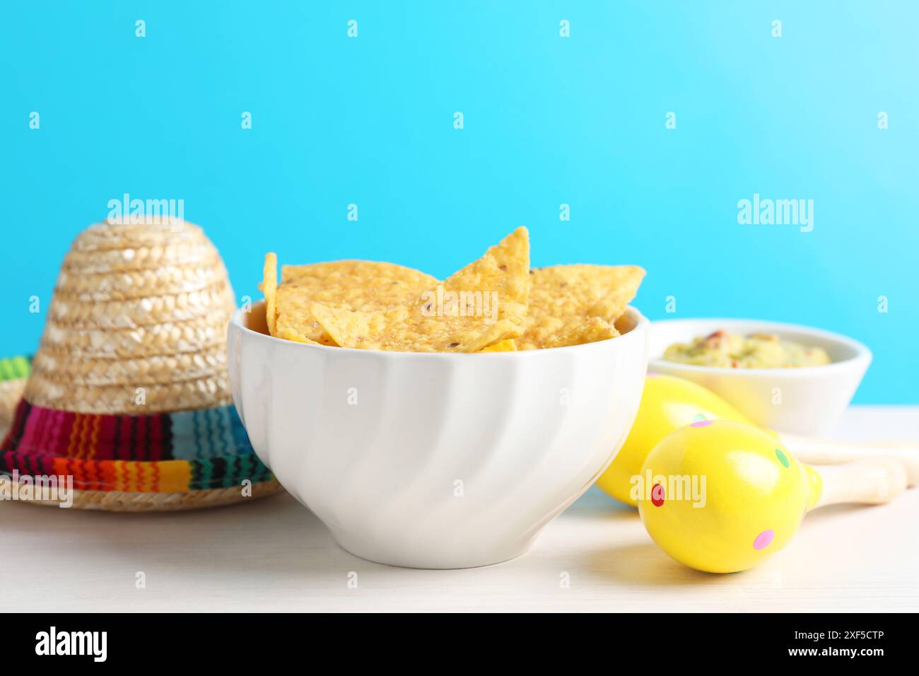 Mexikanischer Sombrero-Hut, Nachos-Chips, Guacamole und Maracas auf weißem Holztisch Stockfoto