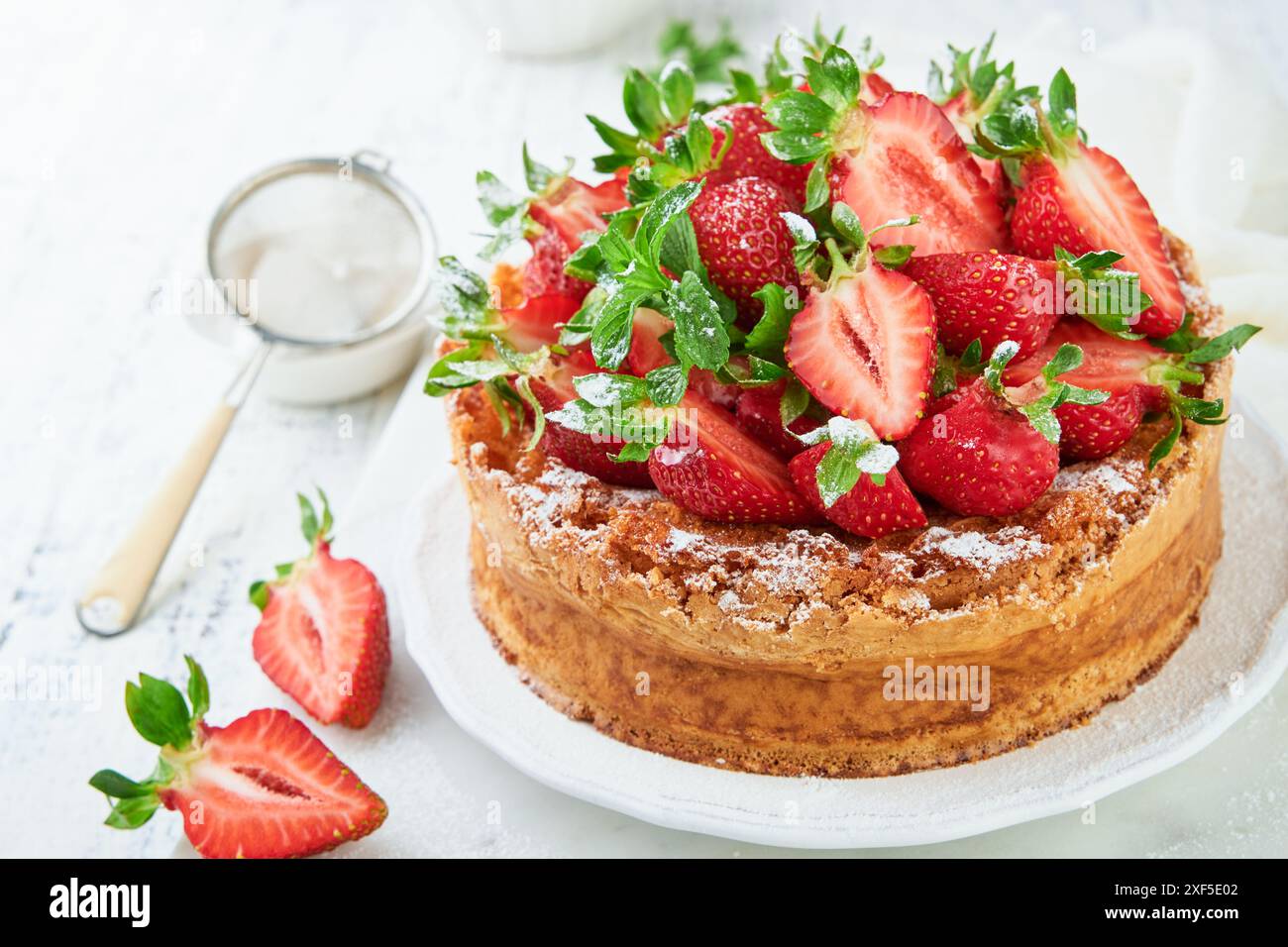 Erdbeerkuchen. Hausgemachter und köstlicher Erdbeer-Biskuitkuchen mit frischen Sommerfrüchten, Frischkäsezuckerguss und Zuckerpulver auf weißem Marmor Stockfoto