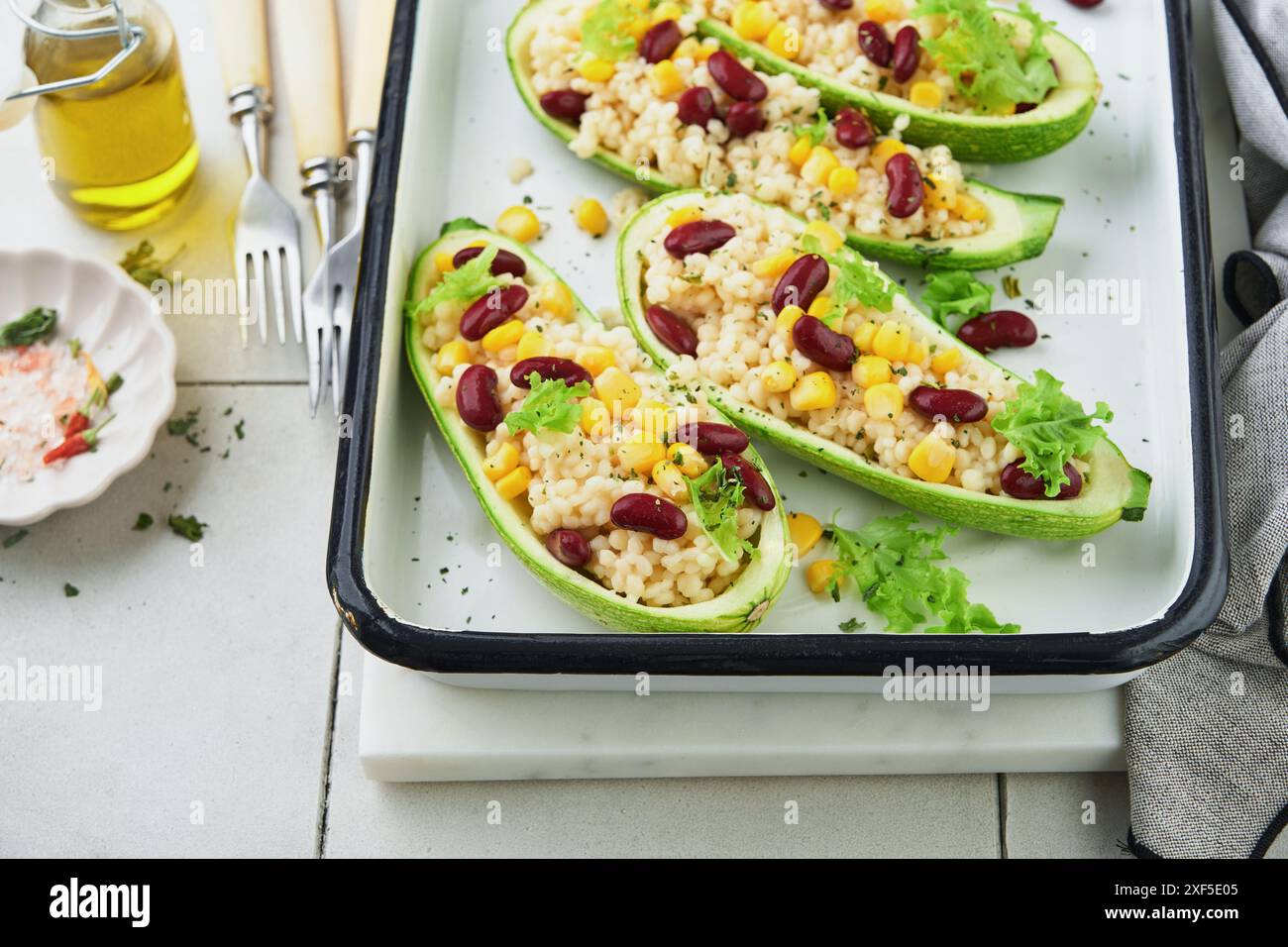 Zucchini gefüllt mit Petitim, roten Bohnen, Mais mit Basilikum und Soße, gebacken auf einem alten, zerrissenen Fliesenhintergrund. Draufsicht. Stockfoto