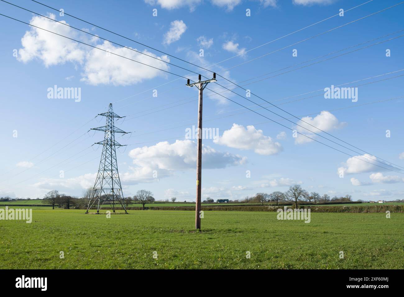 Nationaler Netzstrompylon und Strommast in Großbritannien, auf grünem Feld vor blauem Himmel mit Wolken Stockfoto