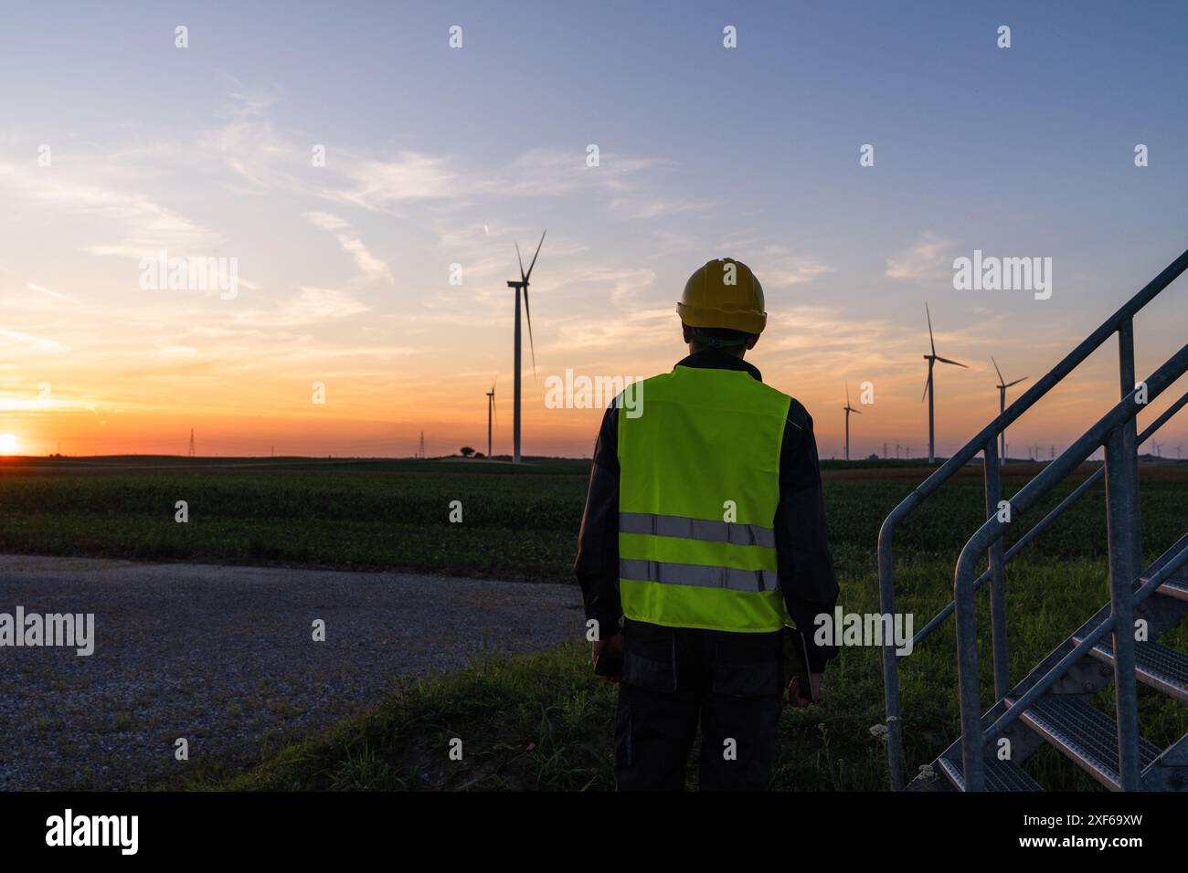 Arbeiter schaut sich Windräder bei Sonnenuntergang an. Stockfoto