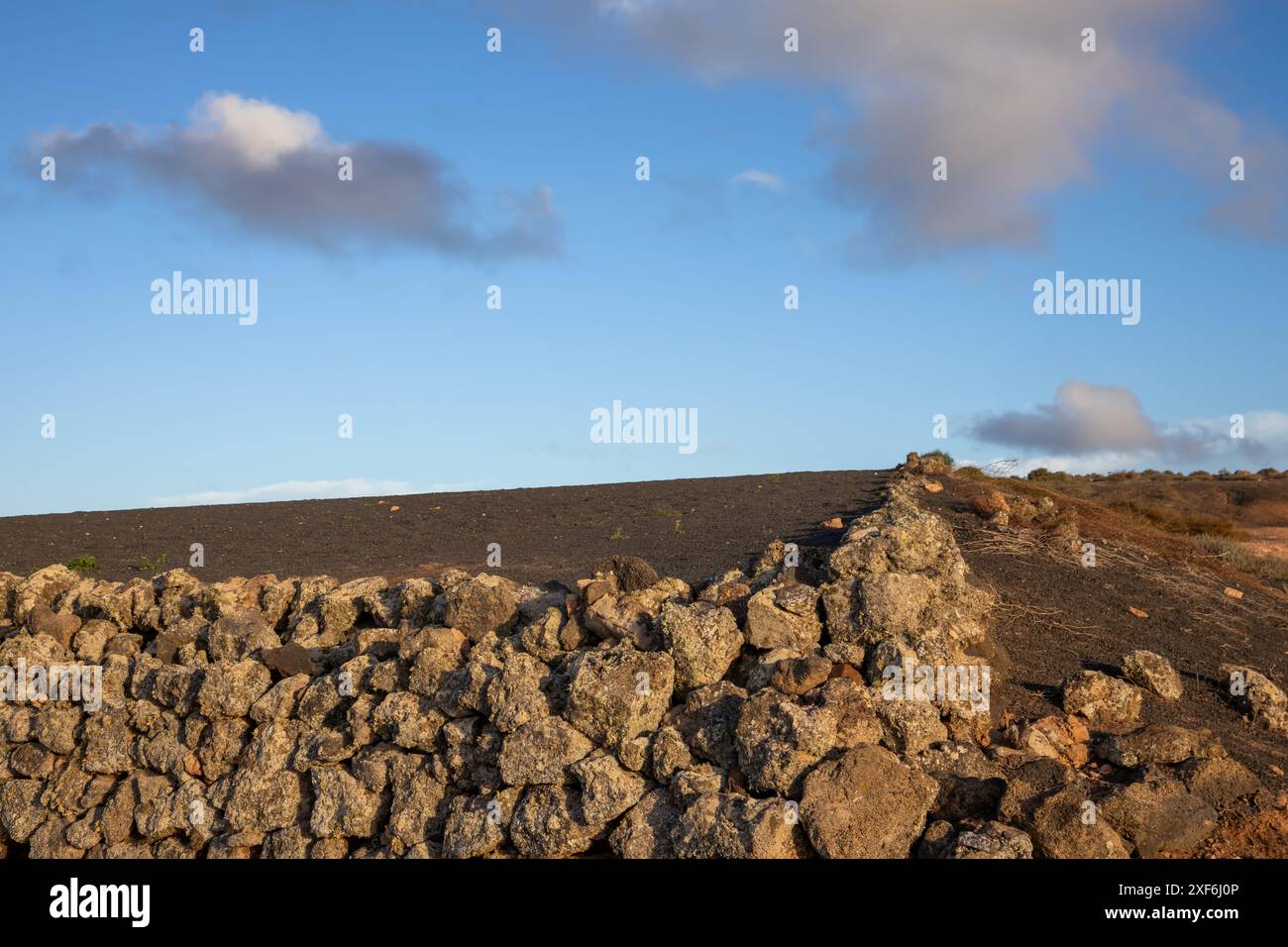 Sandiger Boden, voller Kies und größeren Steinen. Trockener und einsamer Boden. Zaun aus den größten Steinen, die auf dem Feld gefunden wurden. Blauer Himmel mit weißem cl Stockfoto