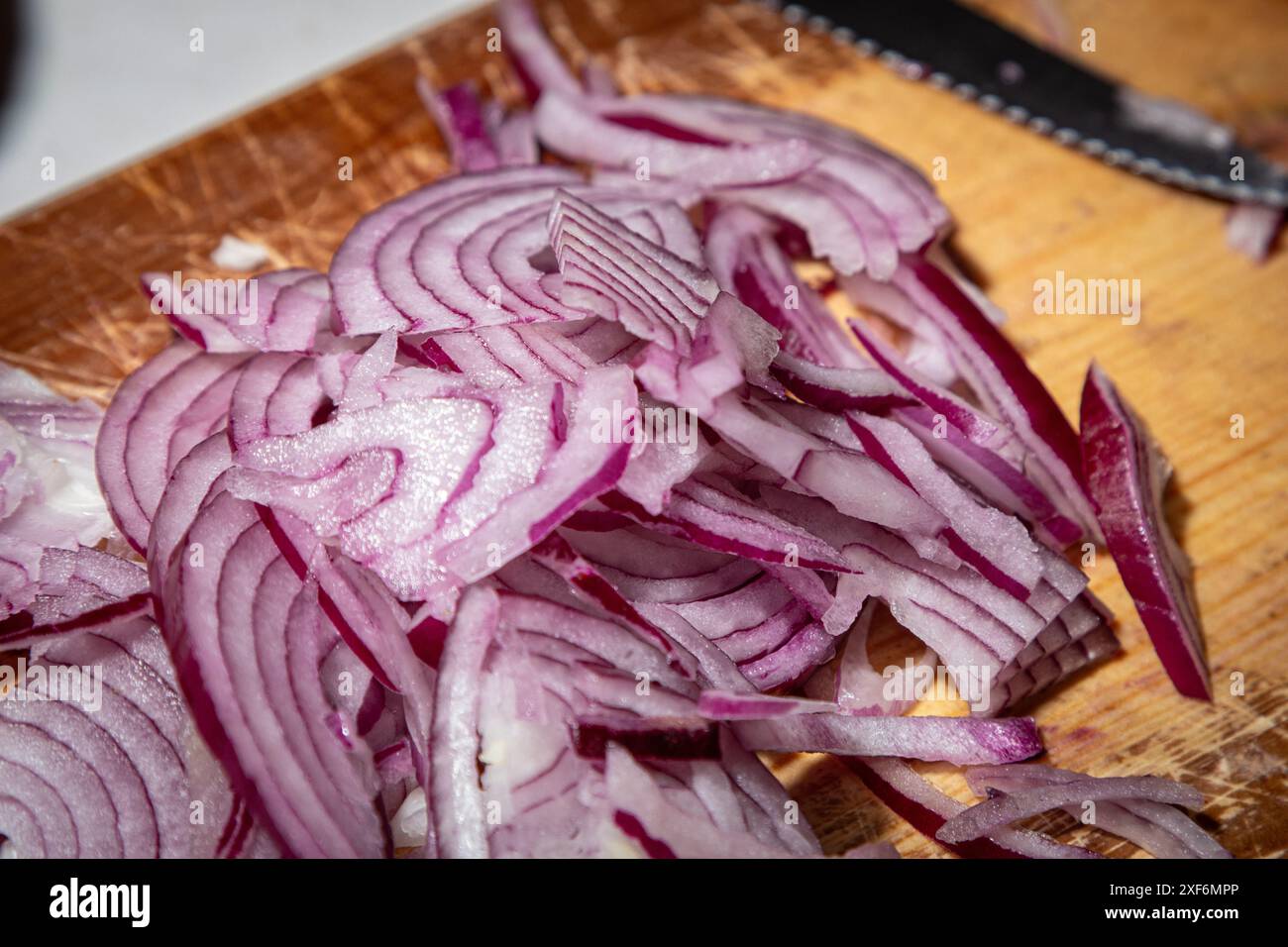 Scheiben von roten Zwiebeln, die zu den Chilis hinzugefügt werden. Stockfoto