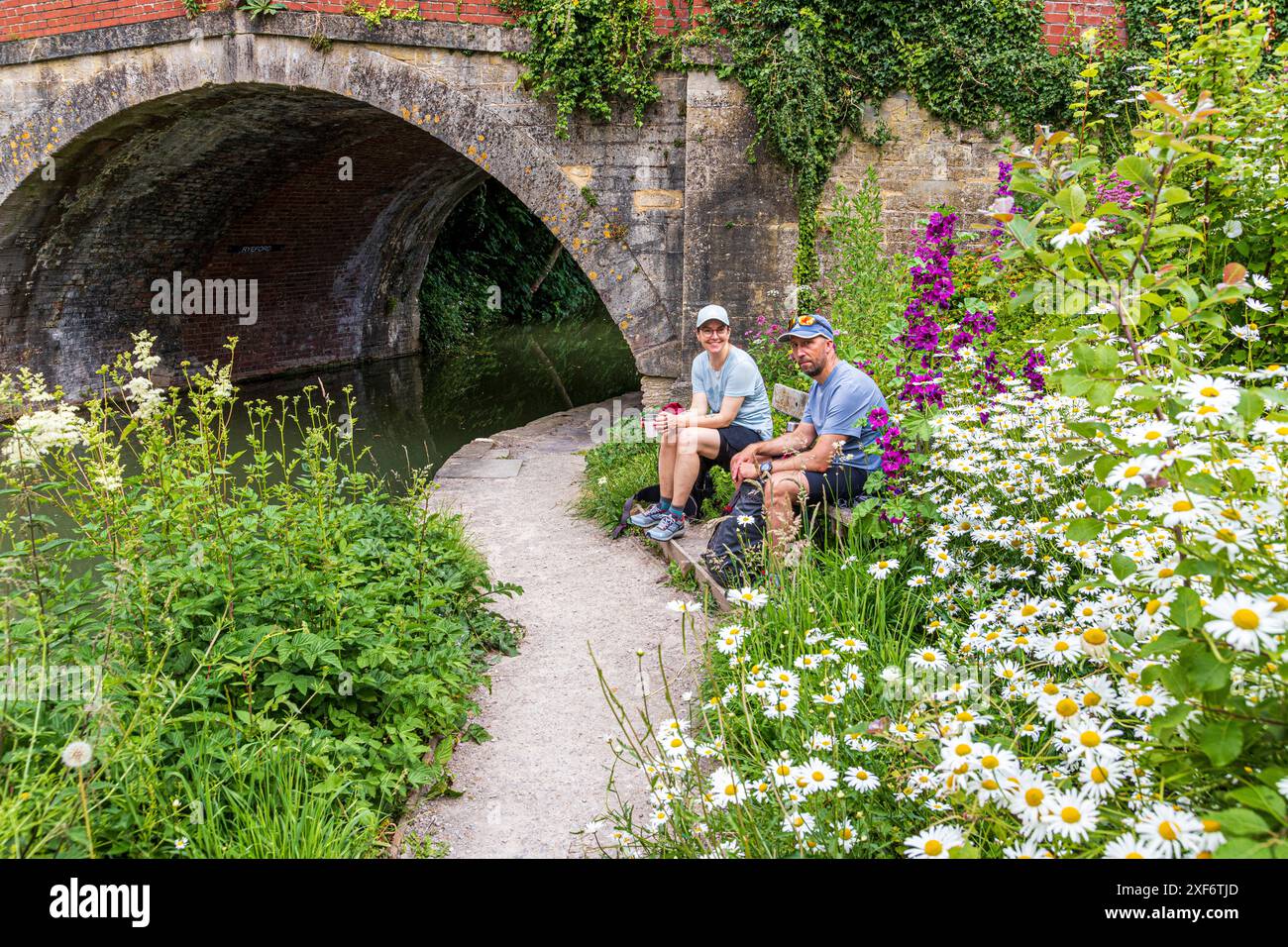 Ein junges Paar aus Schweden, das auf dem Cotswold Way unterwegs ist, genießt eine Pause neben der Brücke über die Stroudwater Navigation in Ryeford bei Stonehouse UK Stockfoto