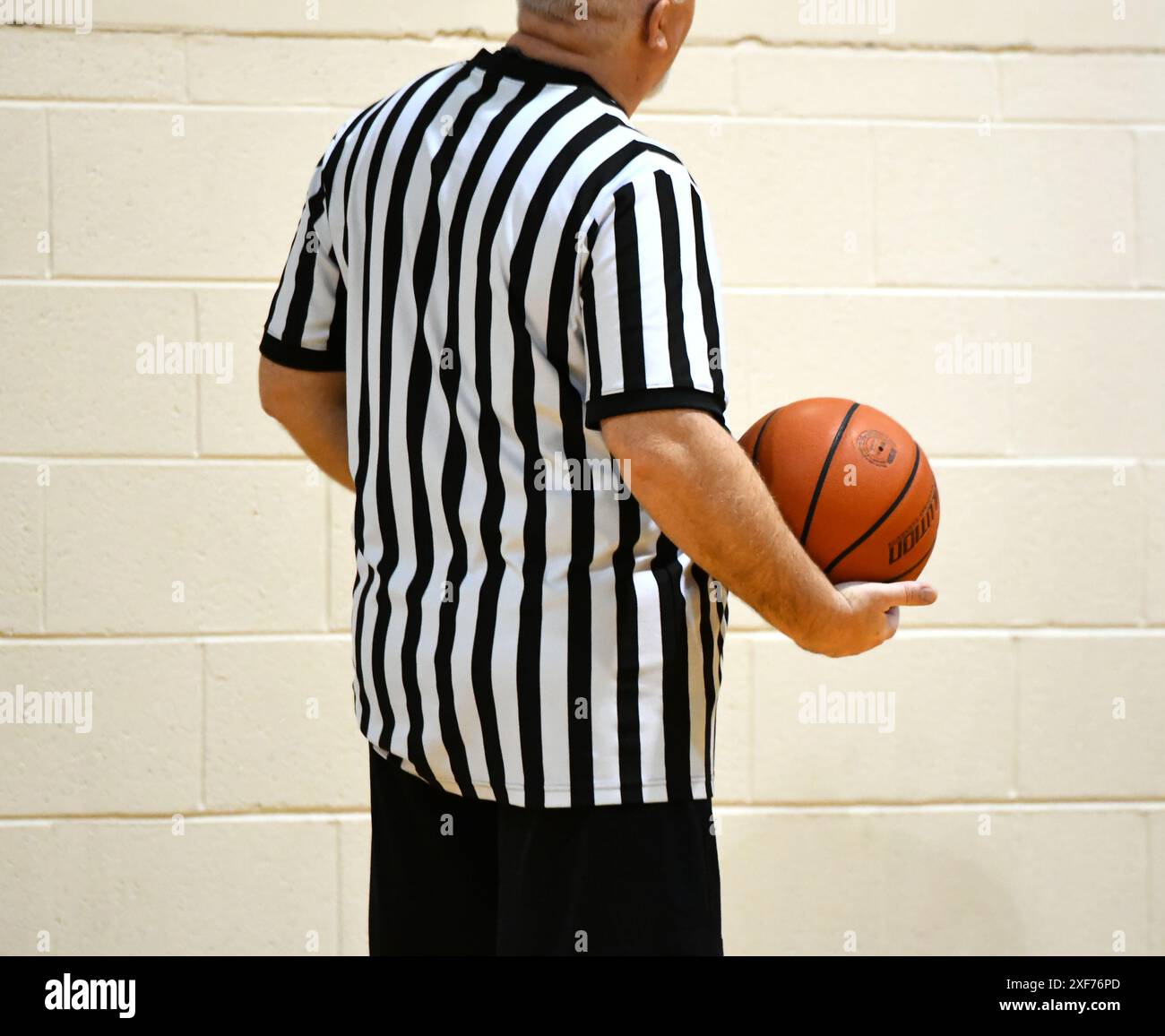 Der Schiedsrichter hält einen Basketball in einer Hand. Er trägt die schwarz-weiß gestreifte Uniform. Stockfoto