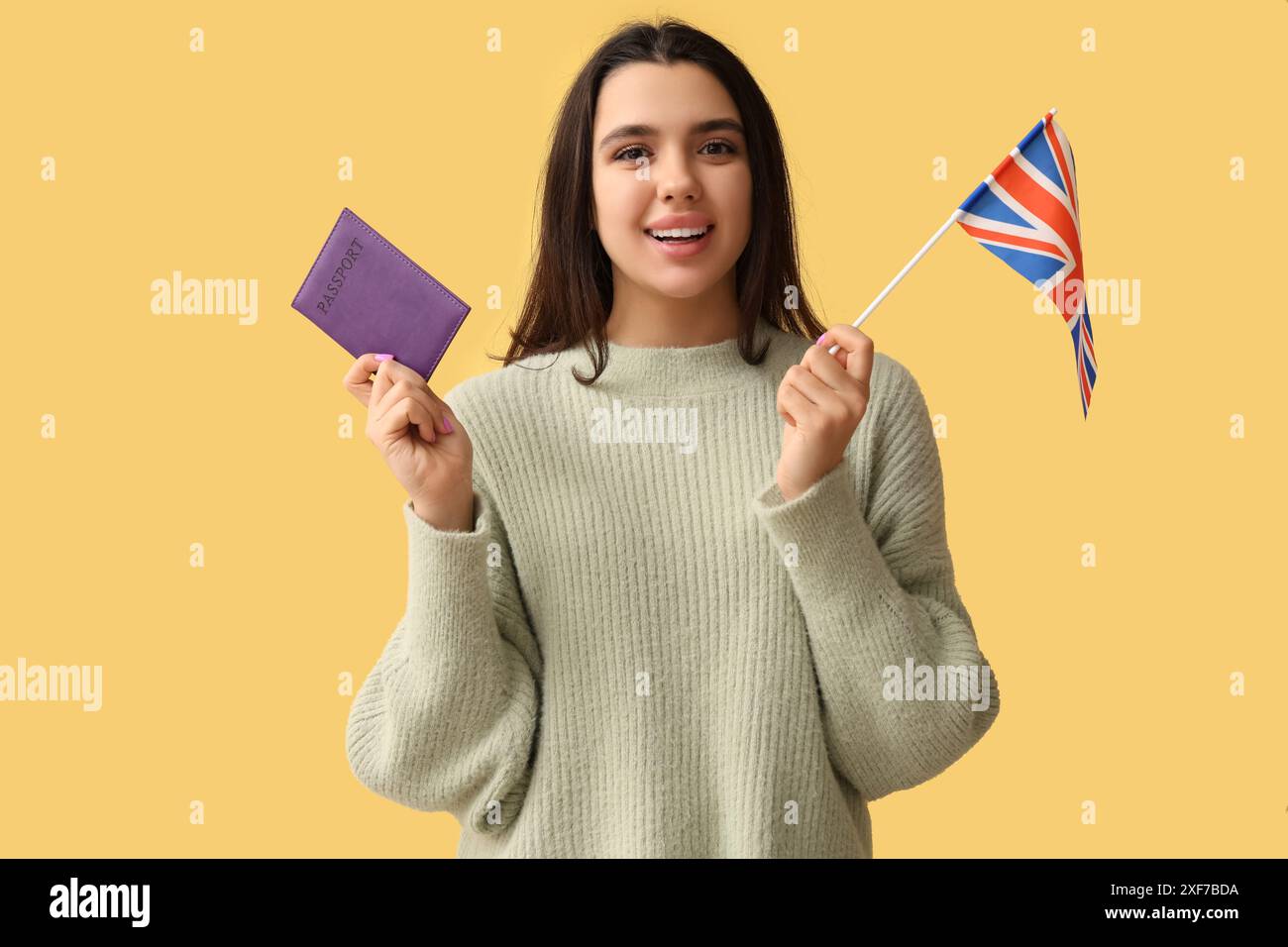 Schöne junge glückliche Frau mit britischer Flagge und Pass auf gelbem Hintergrund Stockfoto