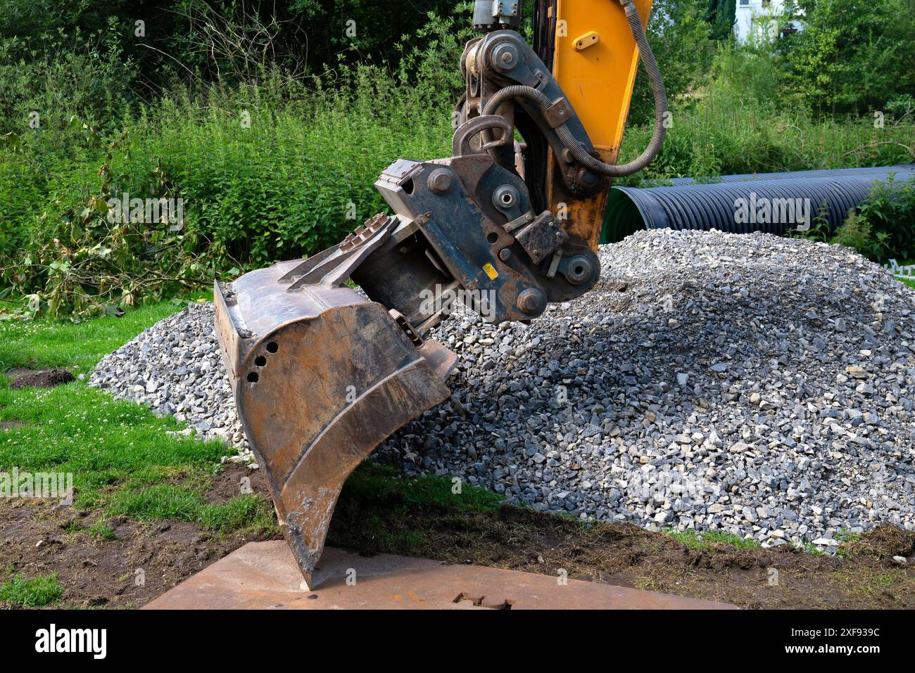 Der Baggerlöffel steht über einem Schotterhaufen, ein schwarzes Abflussrohr im Hintergrund. Stockfoto