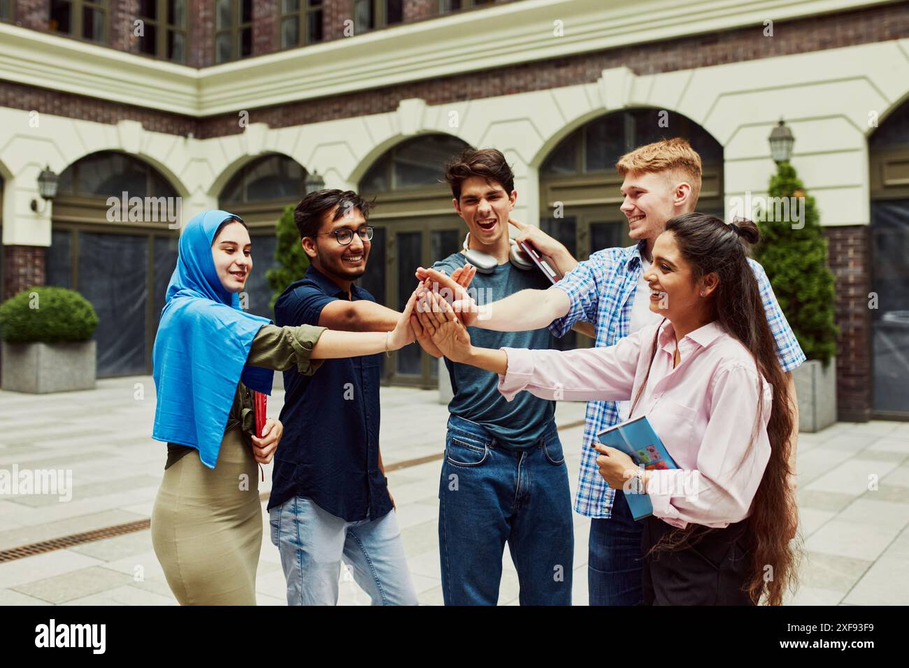Kaukasische, arabische, indische und muslimische Menschen, multirassische Studenten, die außerhalb der Universität stehen und interagieren, um sich auf ein gemeinsames Projekt vorzubereiten. Stockfoto