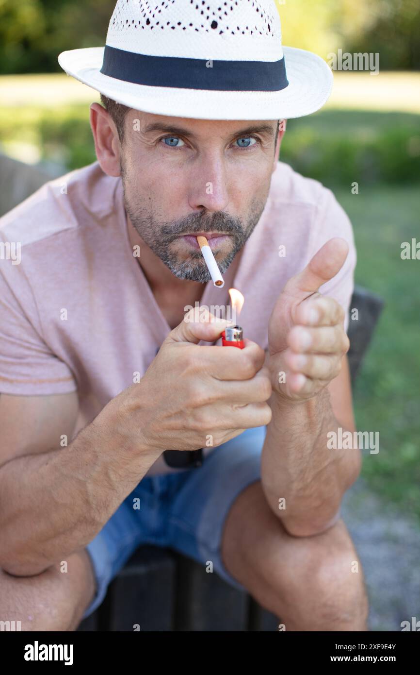 Ein Mann, der eine Zigarette auf einer Bank anzündet Stockfoto